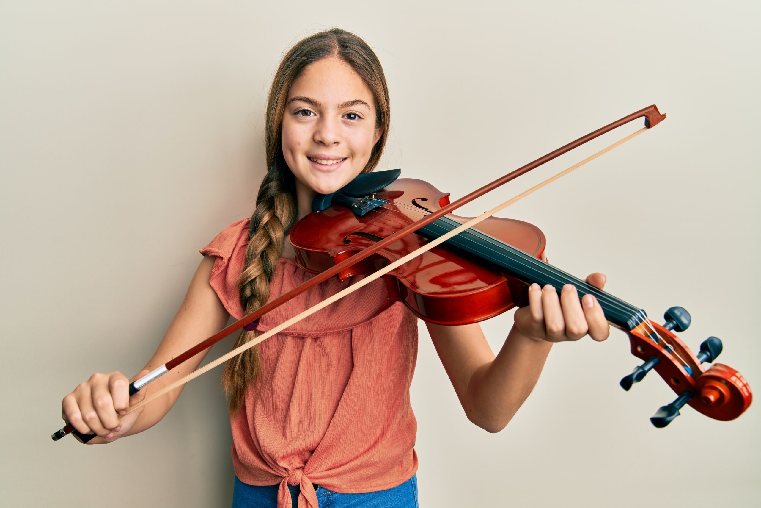 Beautiful brunette little girl playing violin smiling with a happy and cool smile on face. showing teeth.
